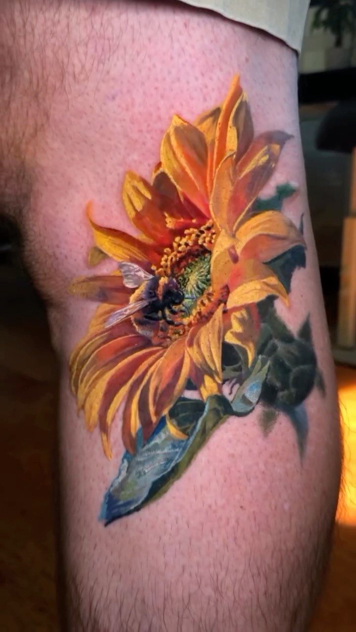Sunflower tattoo with a bee on a person's leg in vibrant yellow and orange