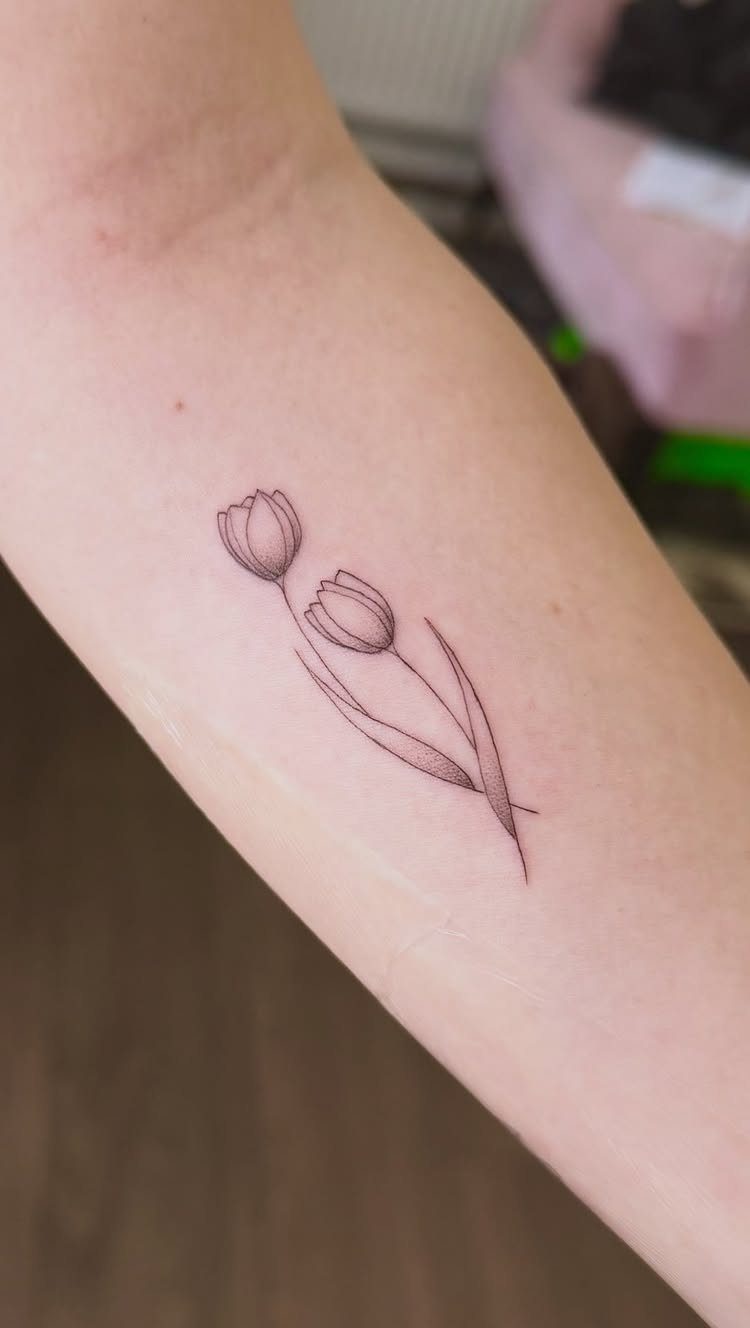 Two minimalist tulip tattoos with fine lines on a person's forearm.