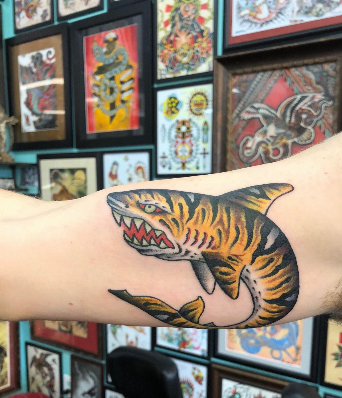 Tiger shark tattoo with orange stripes and sharp teeth on a person's forearm