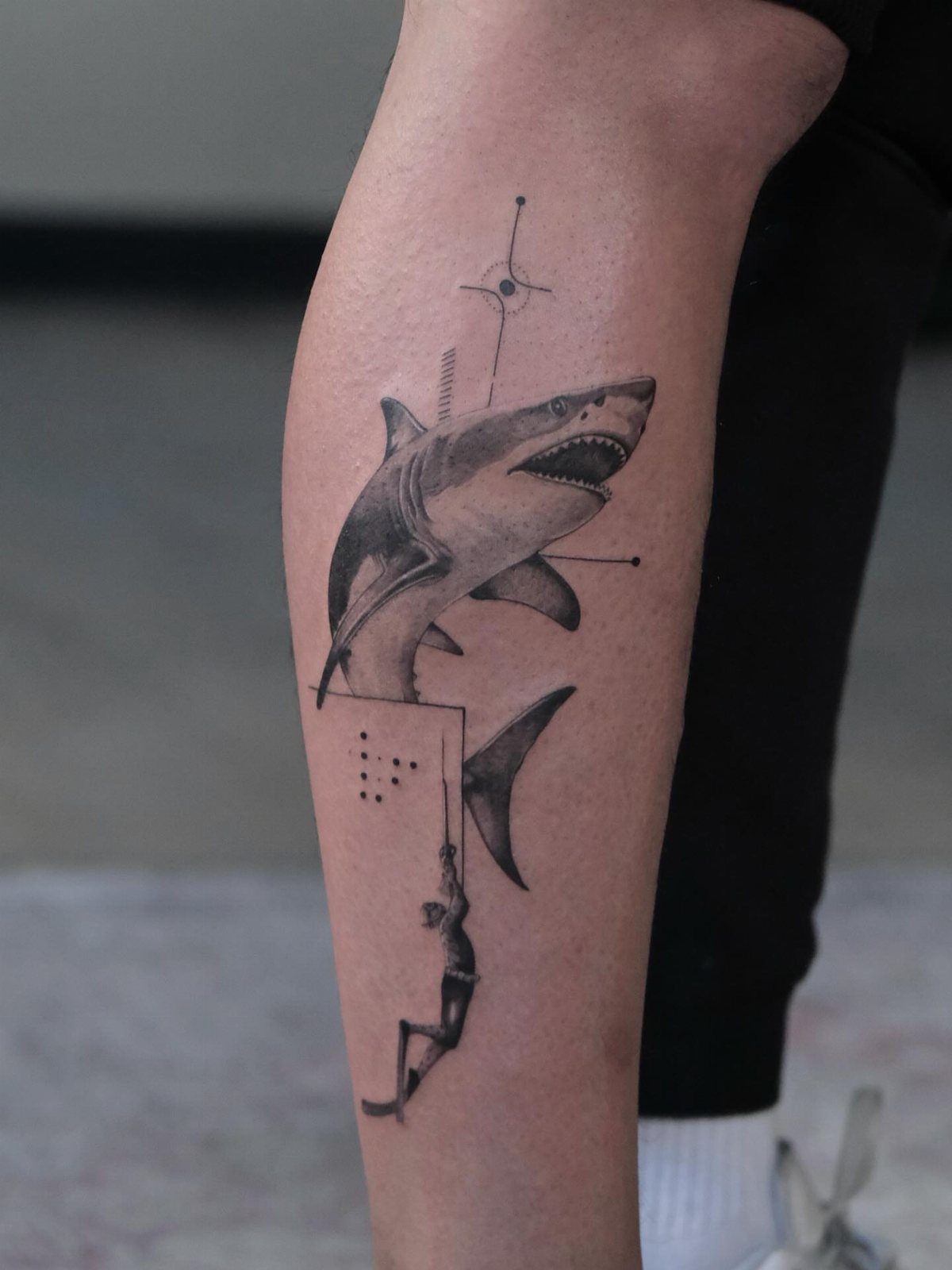 Shark tattoo on a leg with a small human figure and geometric elements