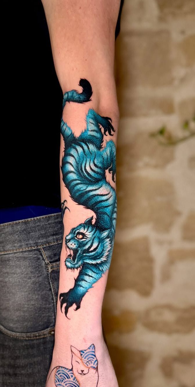 Blue tiger tattoo on a forearm showing a roaring tiger in dynamic motion.
