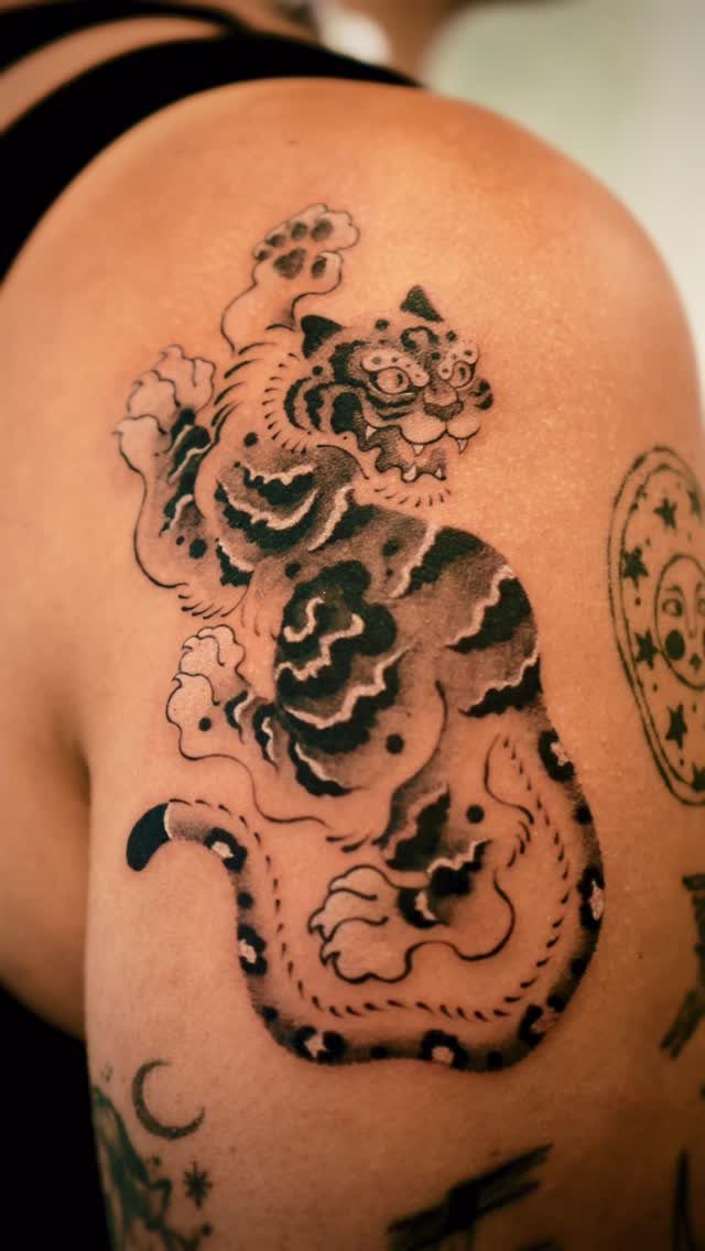 Stylized black and grey tiger tattoo on a person's upper arm shoulder.