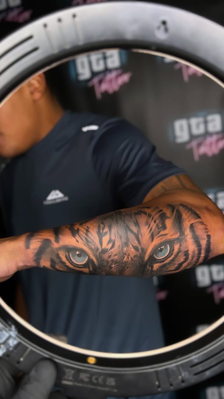 Tiger eyes tattoo on a forearm framed by a circular ring light.