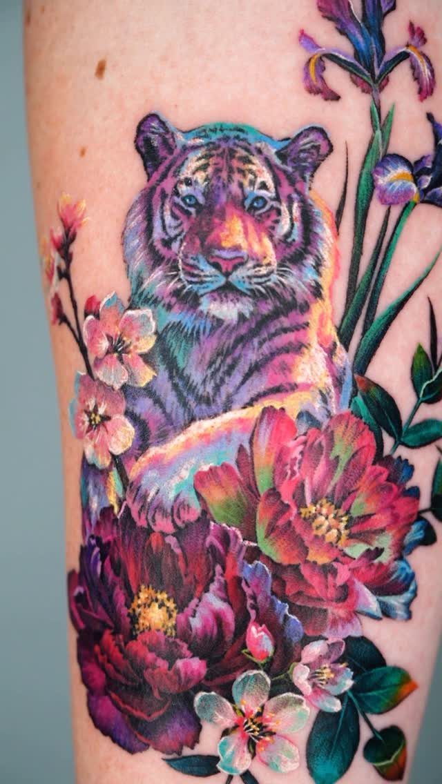 Tiger tattoo surrounded by colorful peonies and irises on human skin.