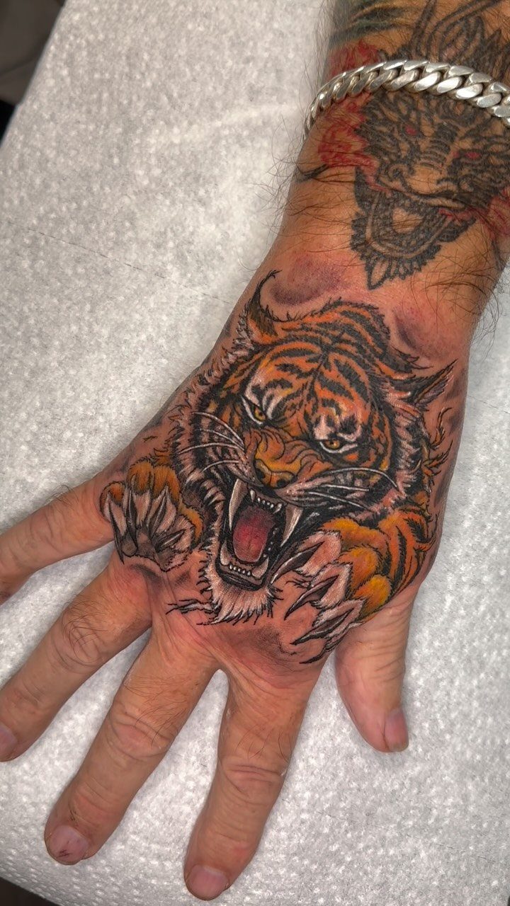 Roaring tiger tattoo with orange stripes covering the back of a person's hand.