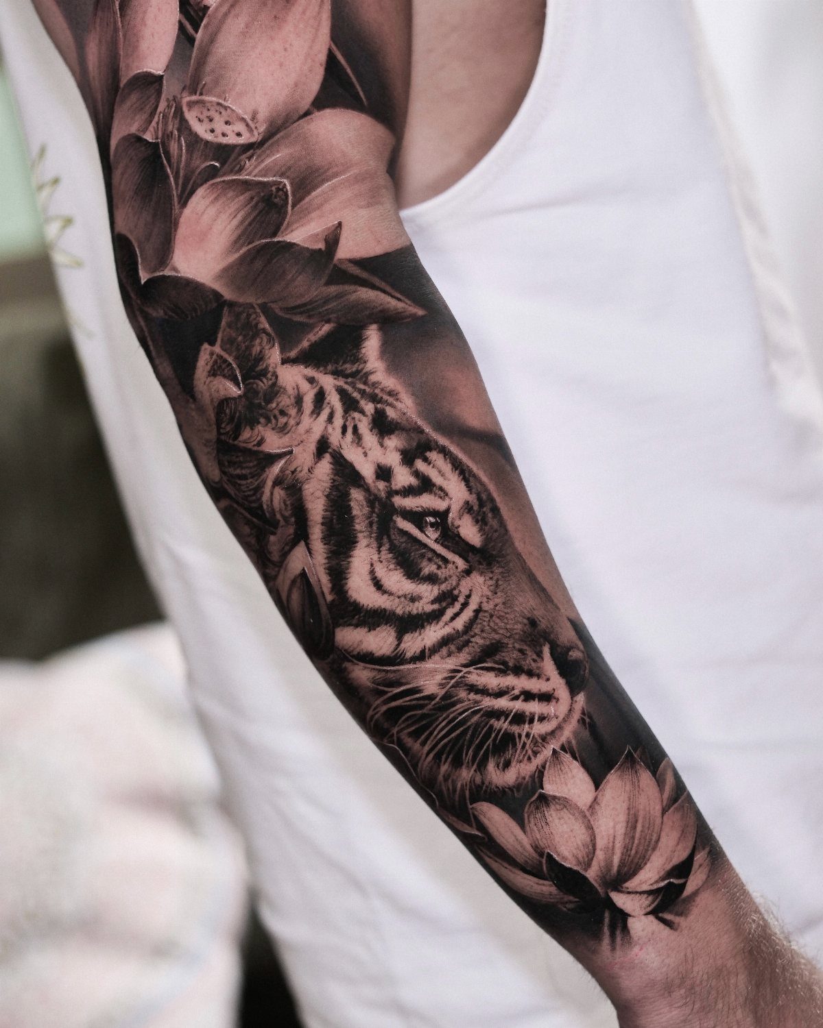 Tiger head and lotus flowers tattoo in black and grey realism on an arm