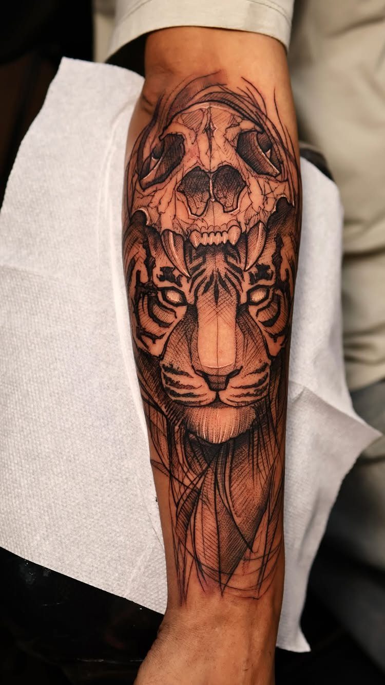 Tiger and skull tattoo on a forearm with detailed black and grey shading.