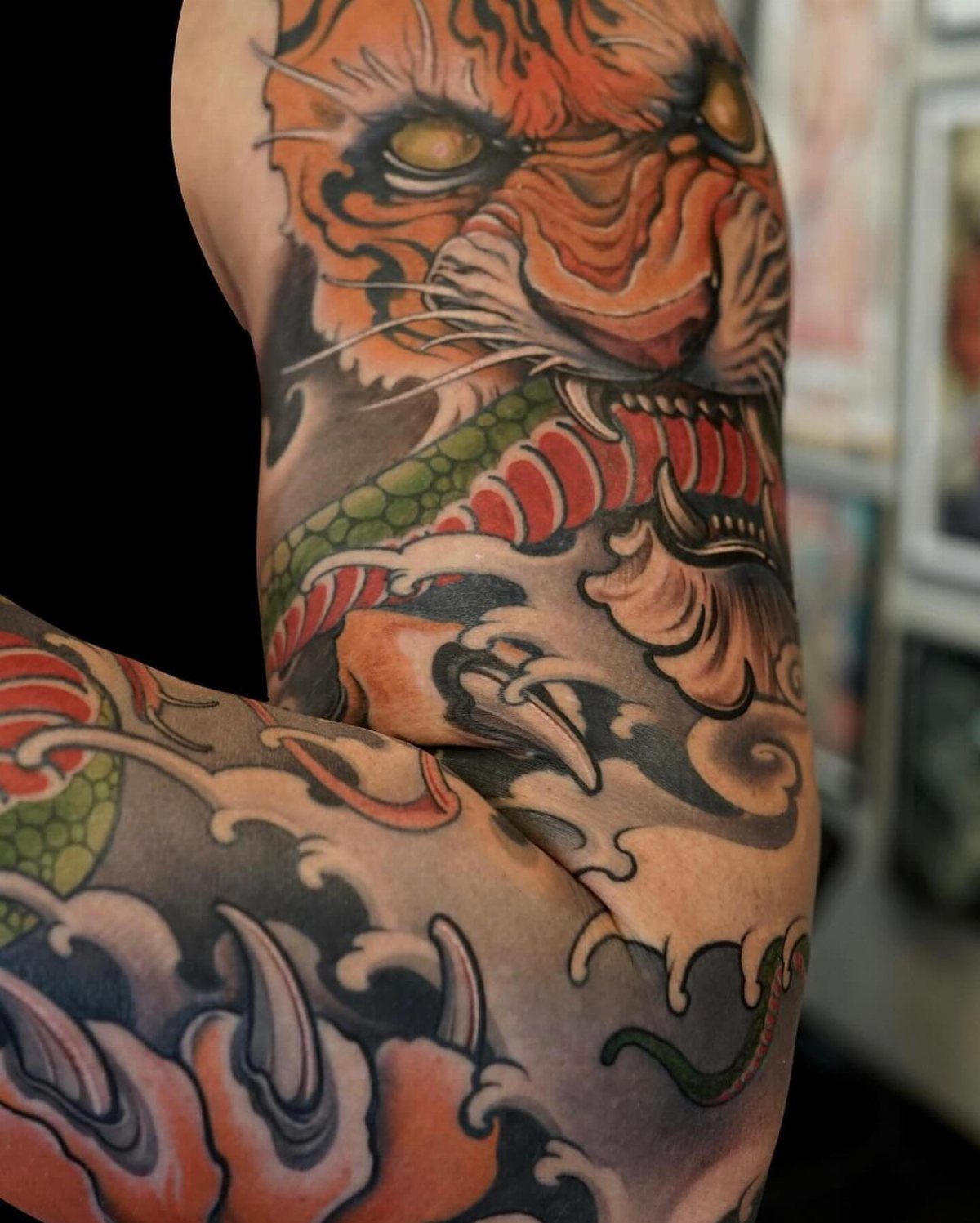 Tiger and snake tattoo on an arm with stylized waves and bold colors