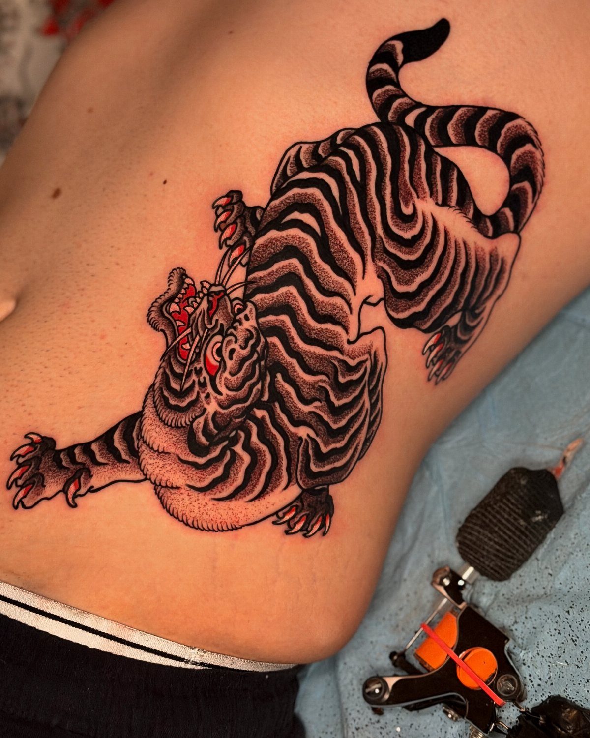 Roaring tiger tattoo with red eyes on a person's side torso