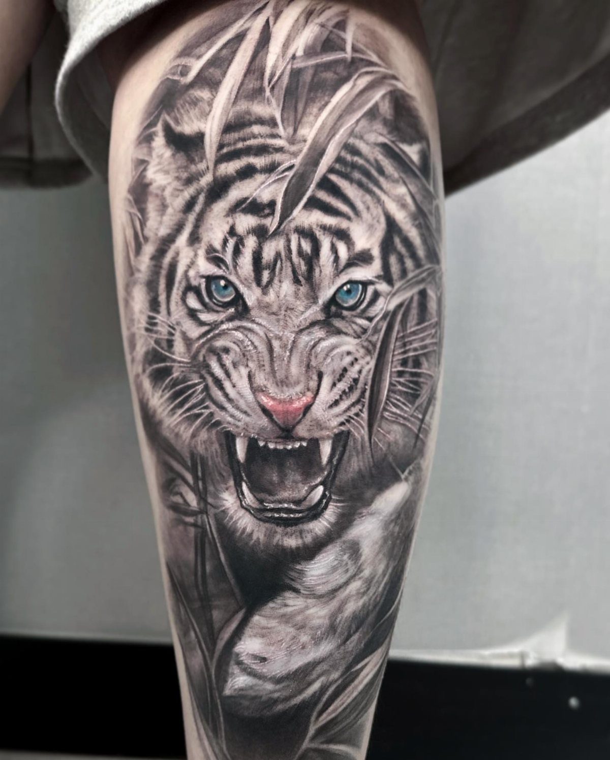 Roaring white tiger tattoo with blue eyes on a person's thigh