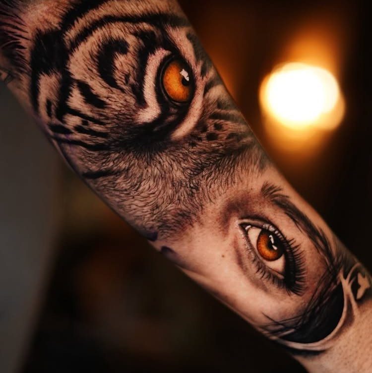Split face tattoo on an arm showing a tiger and human eye.