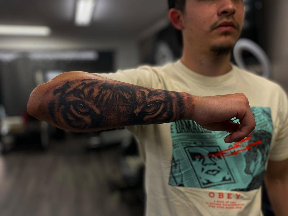 Tiger eyes tattoo on a man's forearm in a blurred indoor setting