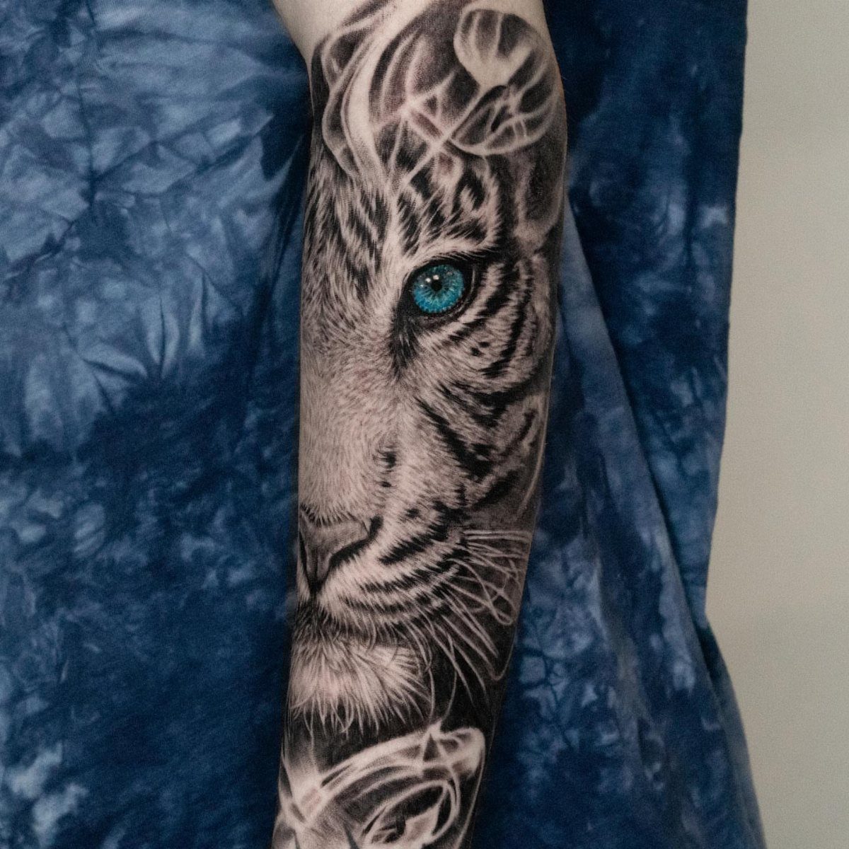 White tiger face tattoo on an arm with a vivid blue eye.