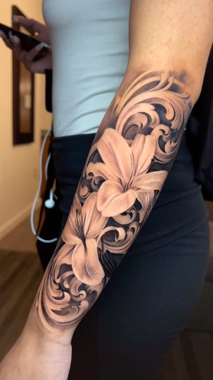 Lily tattoo with ornate swirls on a person's forearm in black and grey ink