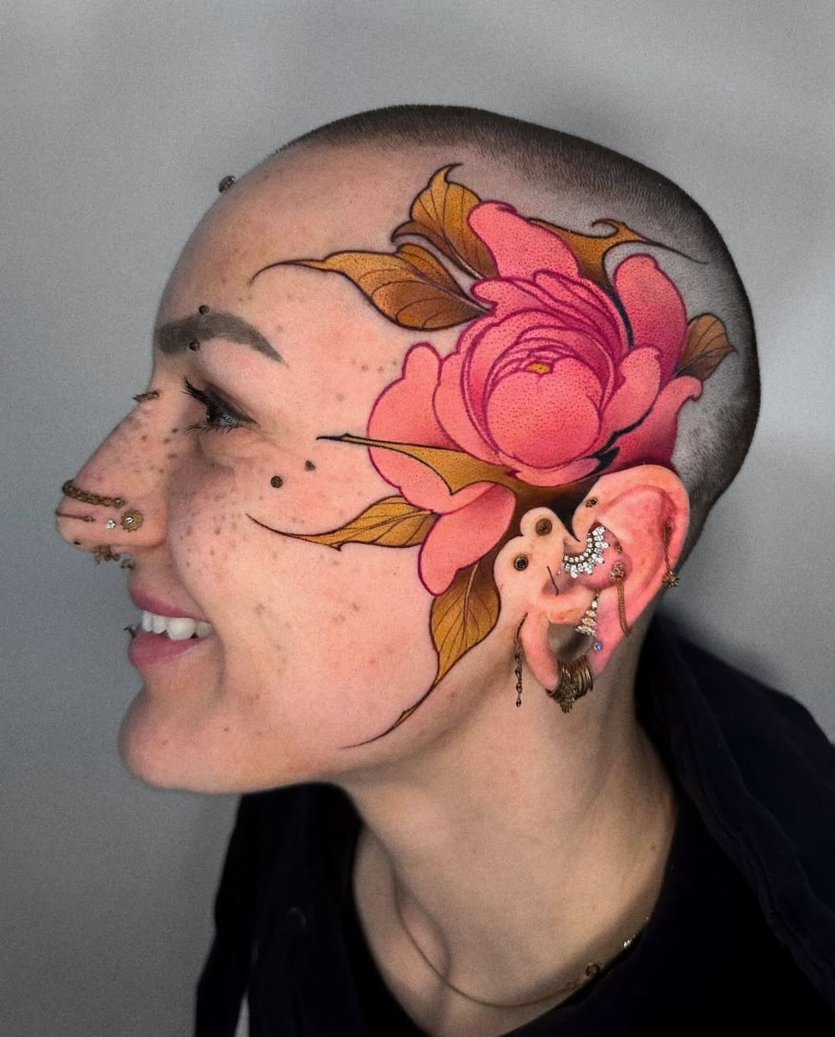 Person with a shaved head featuring a large pink peony flower tattoo.