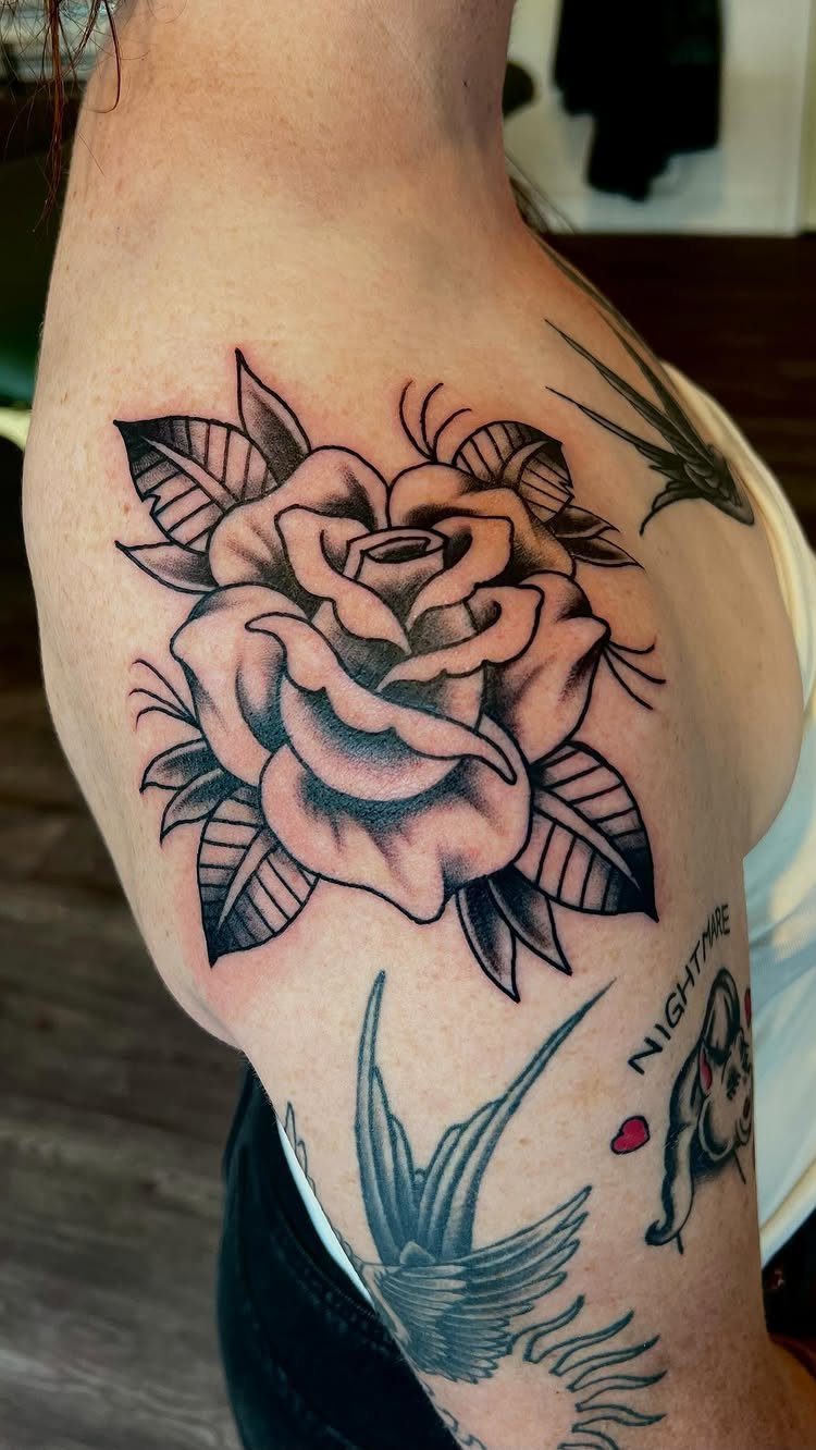 Traditional black and grey rose tattoo with leaves on a person's upper arm.