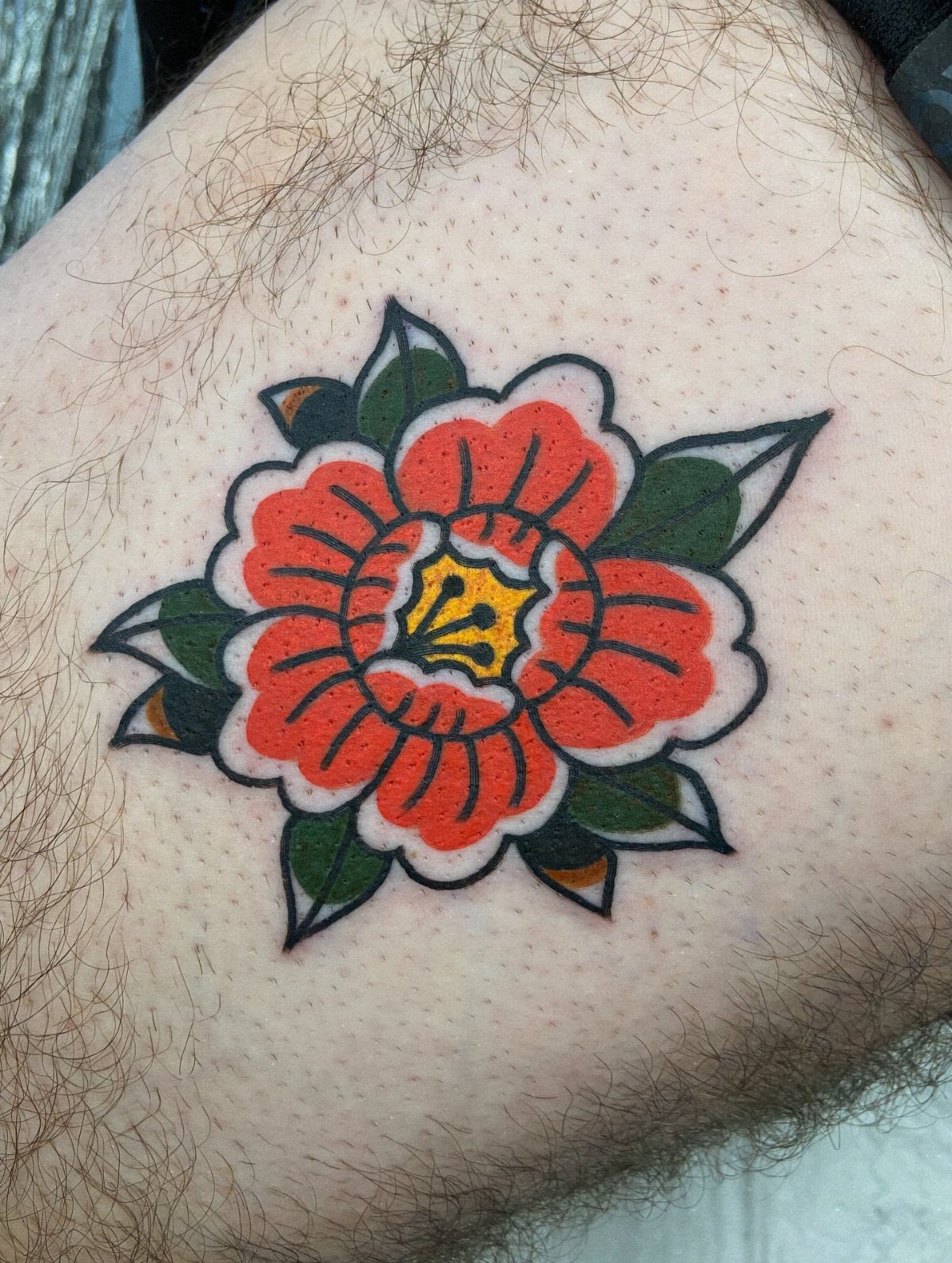 Traditional red flower tattoo with bold outlines and green leaves on skin.