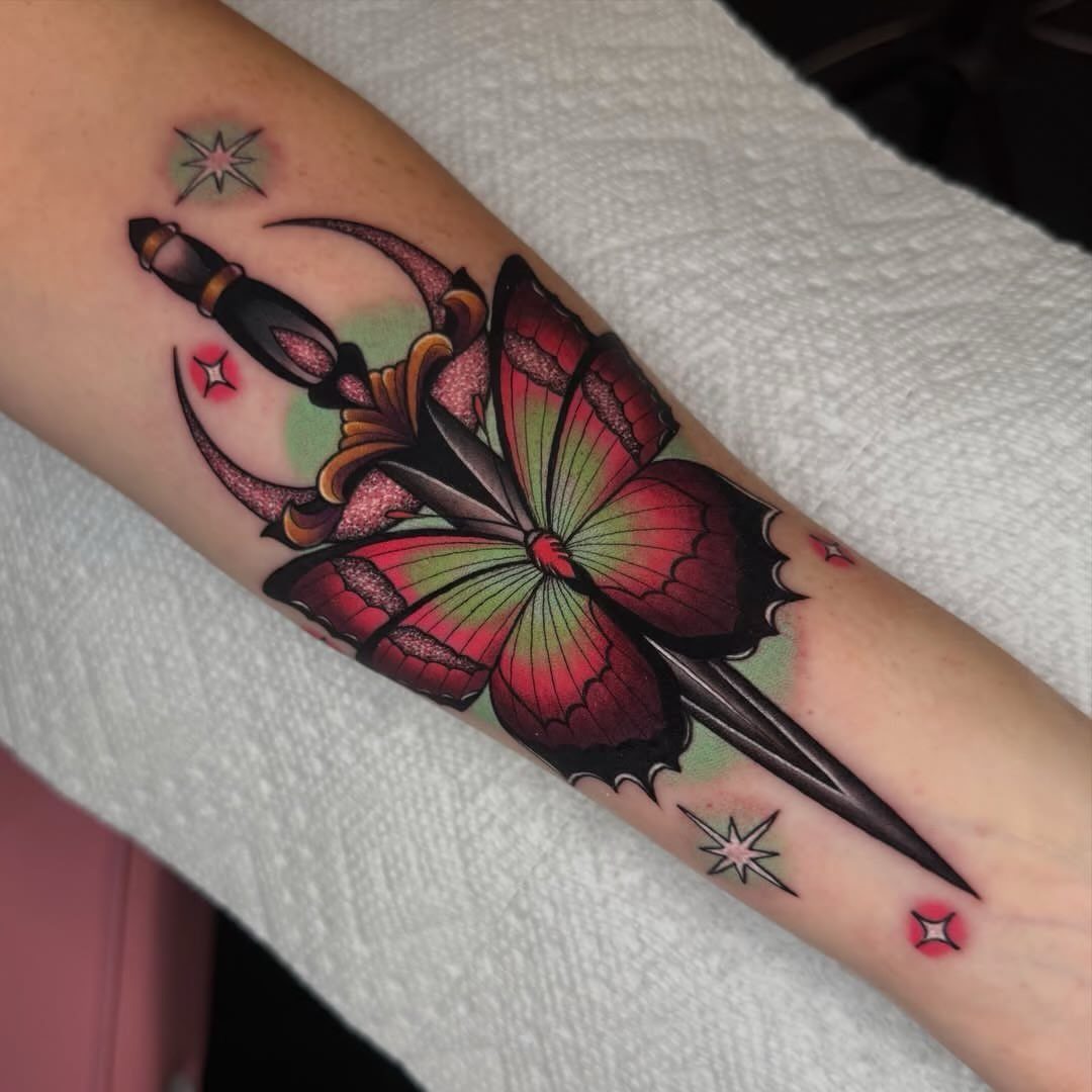 Traditional tattoo of a red butterfly pierced by a dagger on a forearm