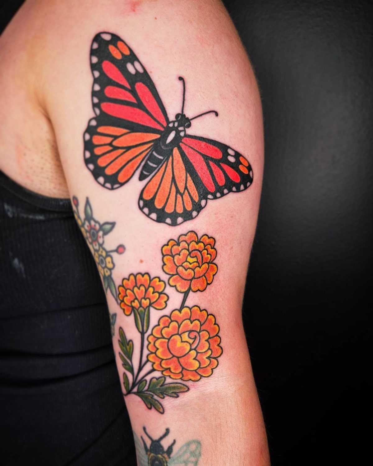 Monarch butterfly tattoo with orange flowers on a person's upper arm