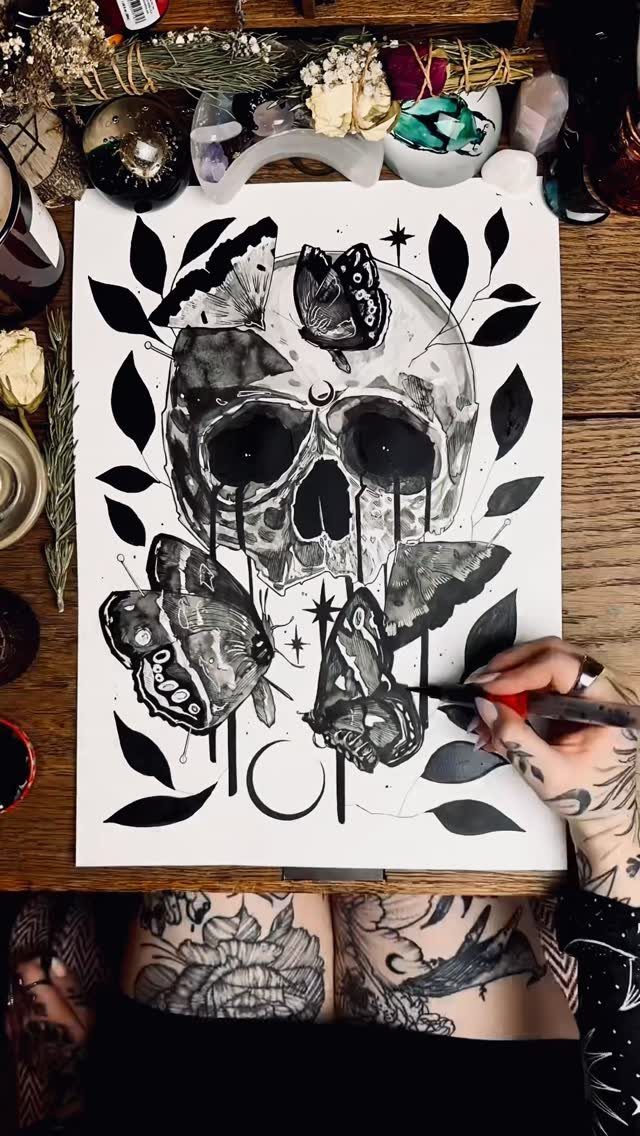 Hand drawing a black and white illustration of a skull and butterflies on paper.