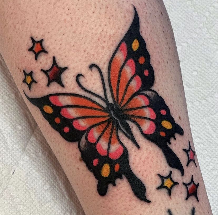 Traditional orange and black butterfly tattoo surrounded by small stars on skin