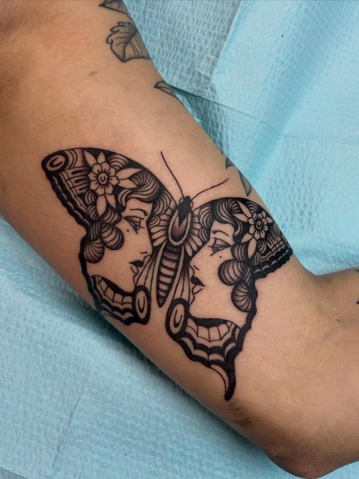 Butterfly tattoo on an ankle with wings shaped like two female faces.