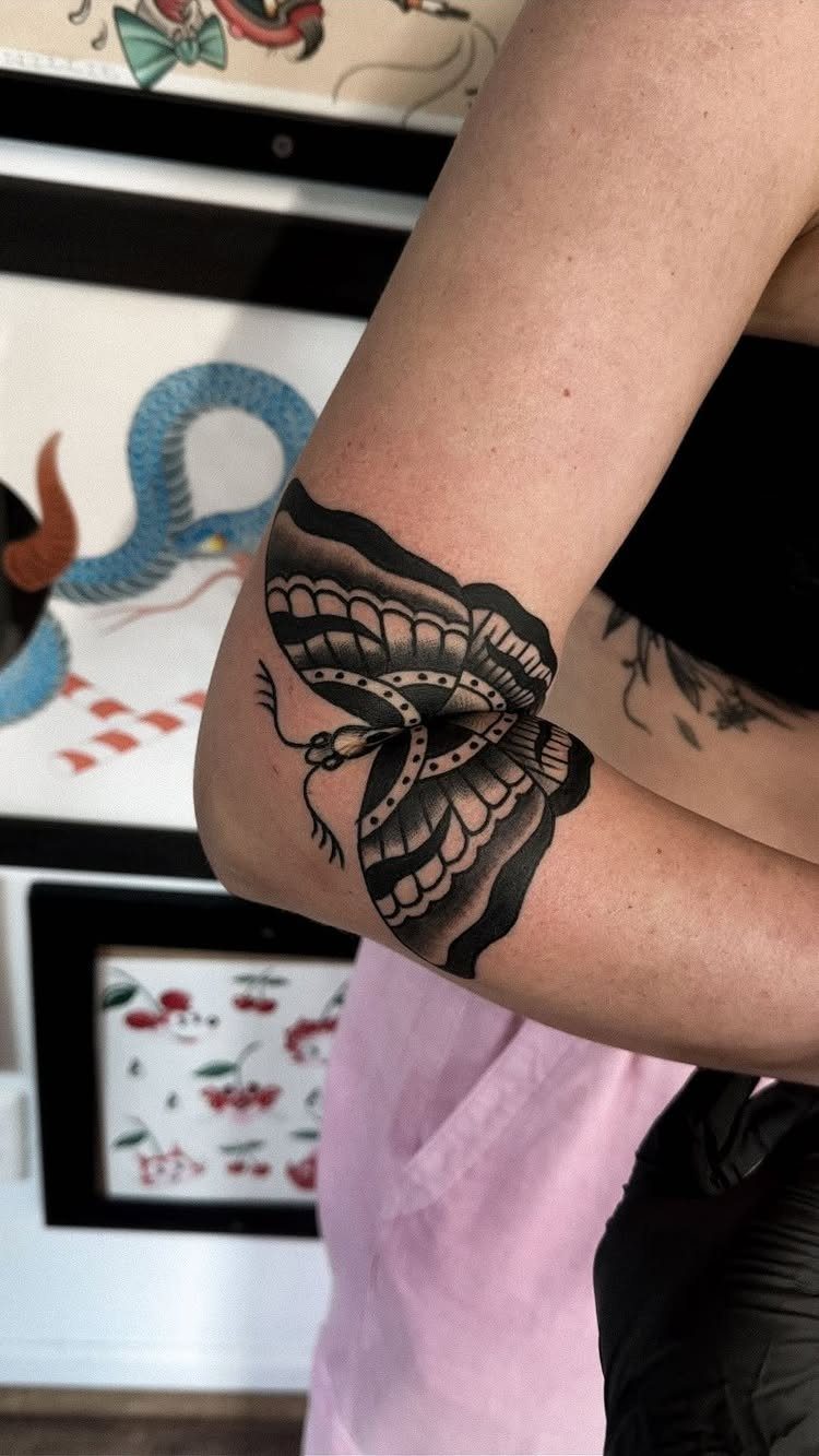 Traditional black and grey butterfly tattoo on a person's elbow with bold outlines.