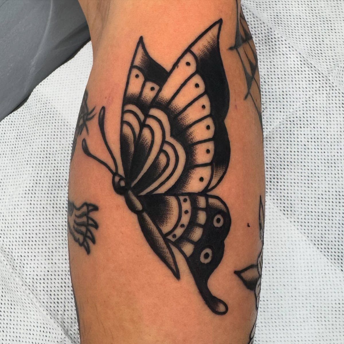 Traditional black ink butterfly tattoo on a person's forearm with bold outlines.