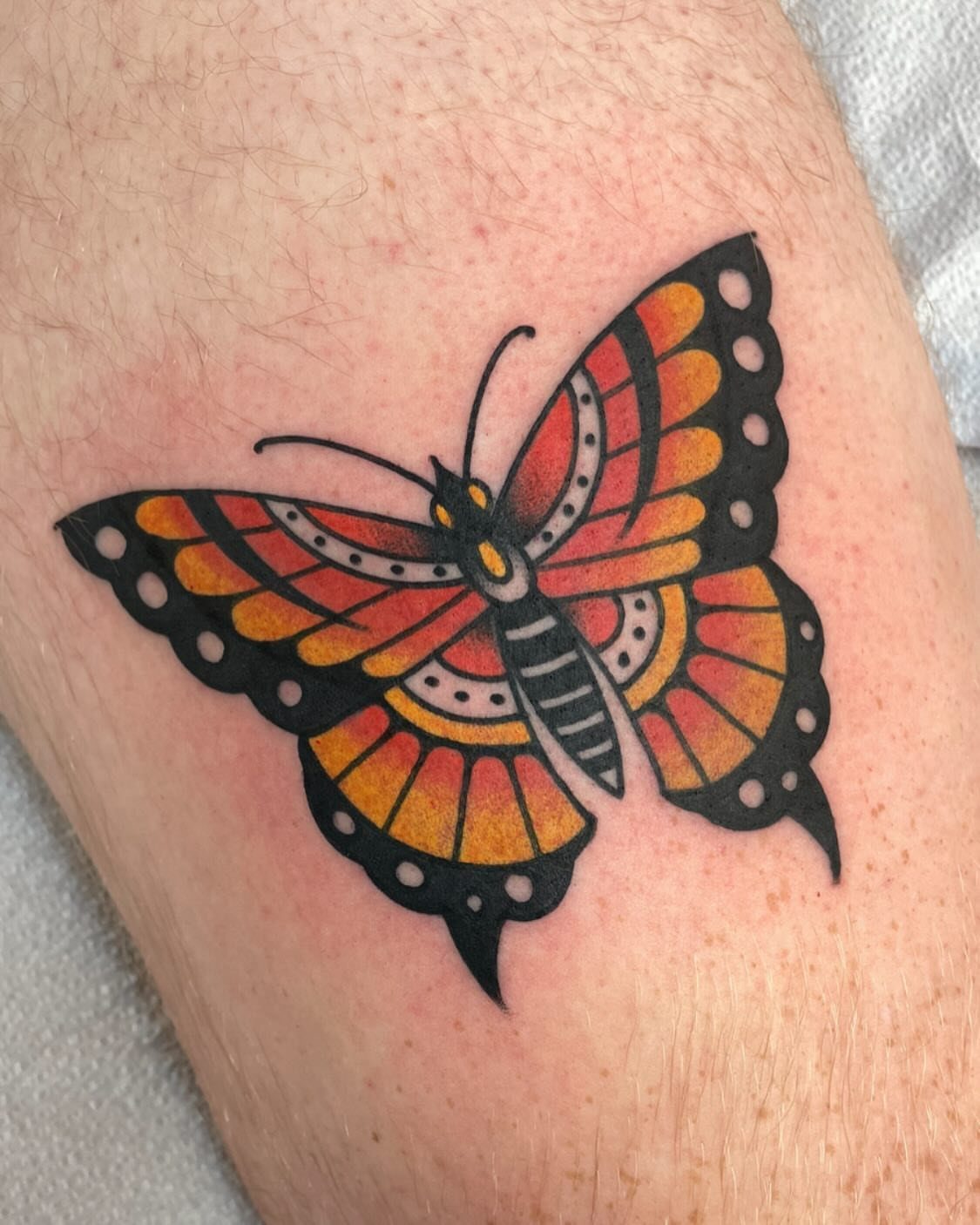 Traditional orange and black butterfly tattoo on a person's skin.