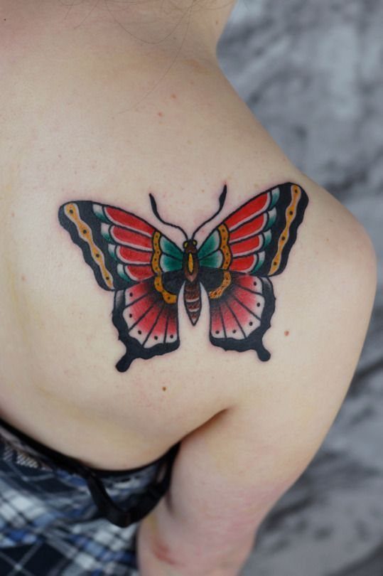 Traditional butterfly tattoo with red and yellow wings on a person's shoulder