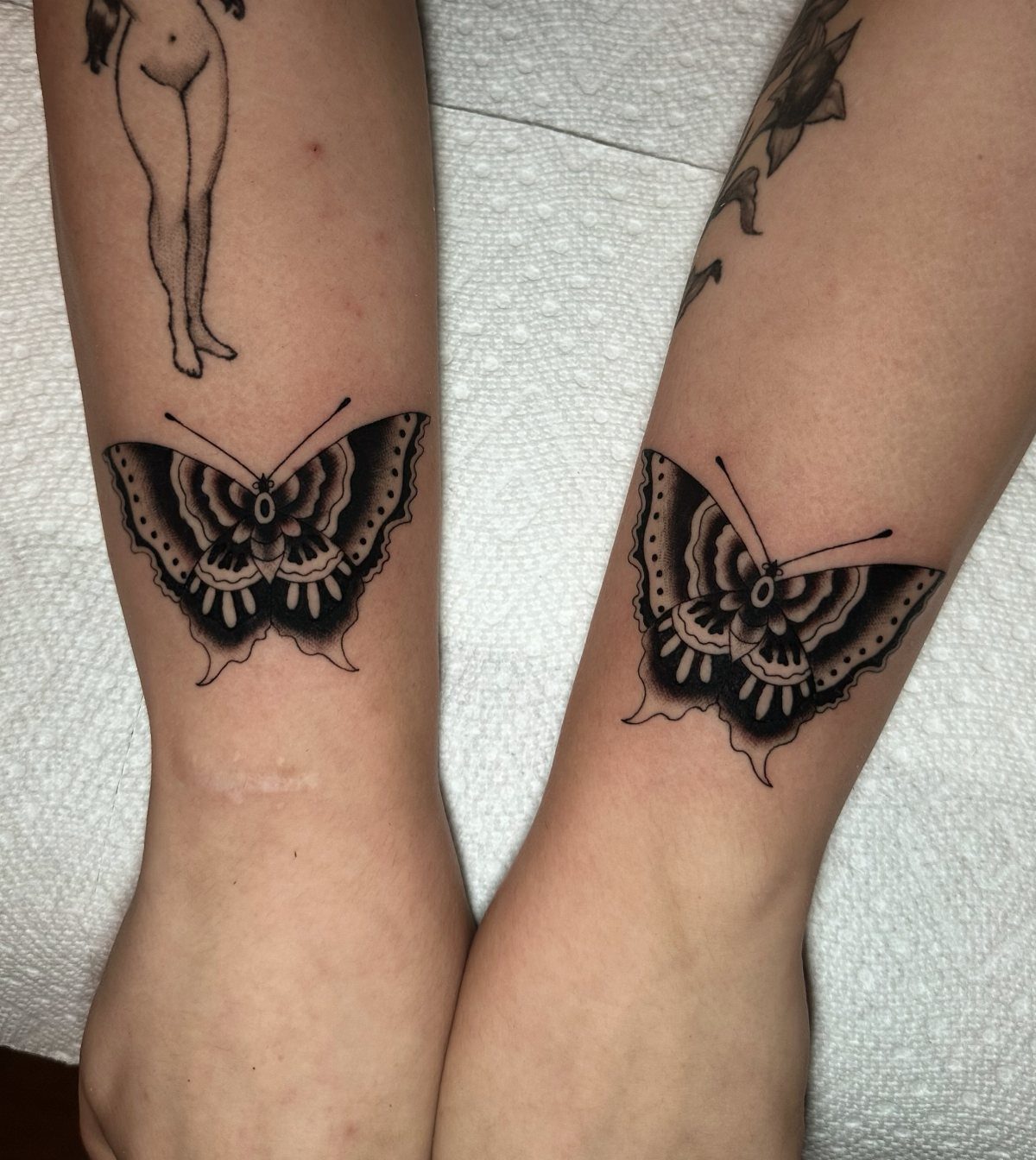Two matching traditional black and grey butterfly tattoos on inner forearms.