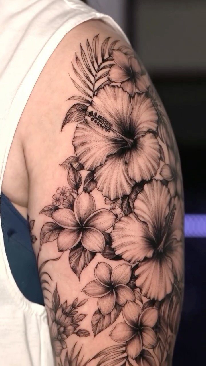 Hibiscus and plumeria flower tattoo with palm leaves on an upper arm.
