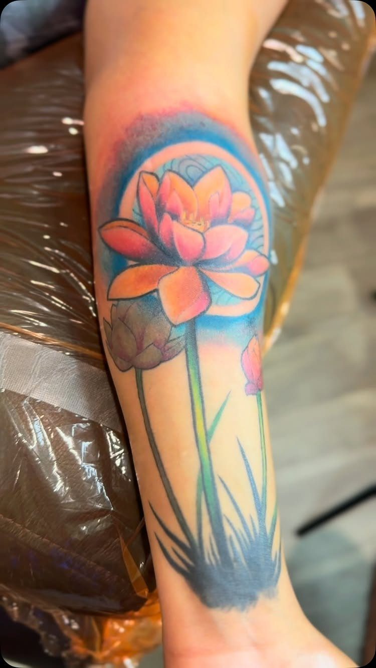 Lotus flower tattoo on a forearm with orange petals and a blue halo.