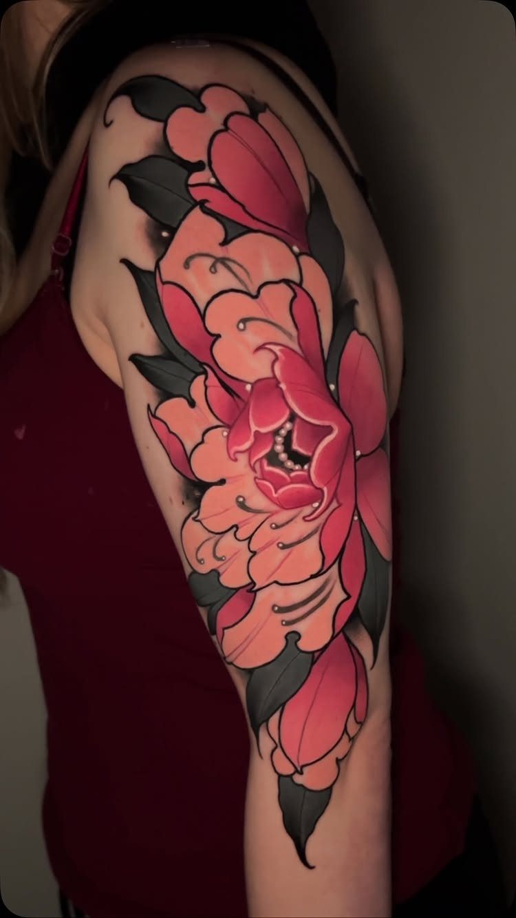 Peony flower tattoo with pink petals and dark green leaves on an upper arm.