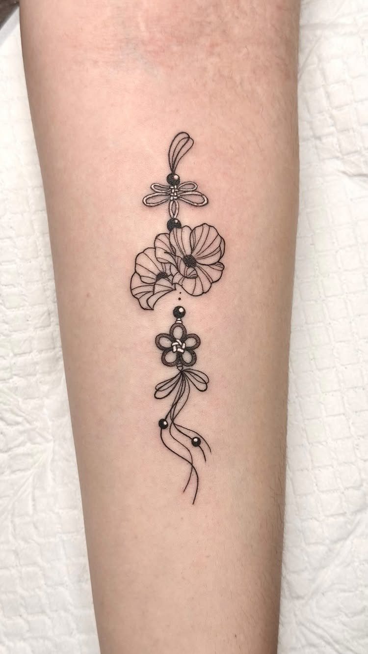 Poppy flower tattoo on an arm with decorative beads and a bow design.