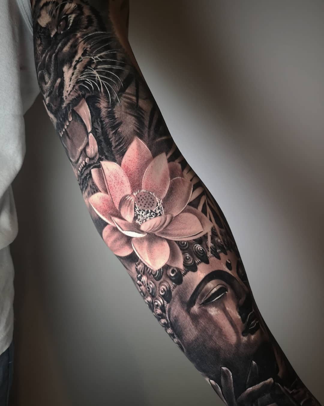 Tattoo on an arm showing a tiger, pink lotus flower, and Buddha face.