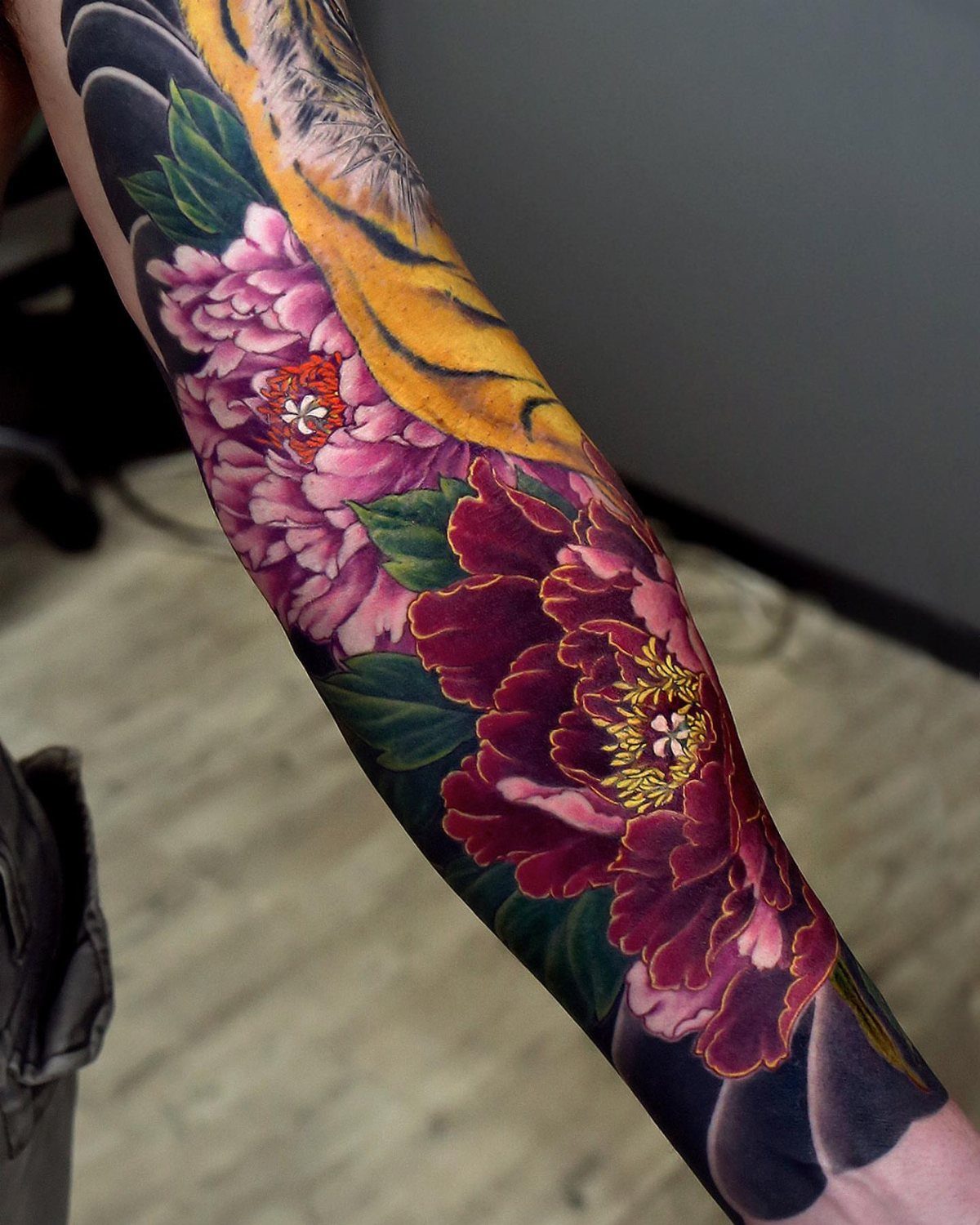 Traditional Japanese tattoo on an arm featuring a yellow tiger and red peonies.