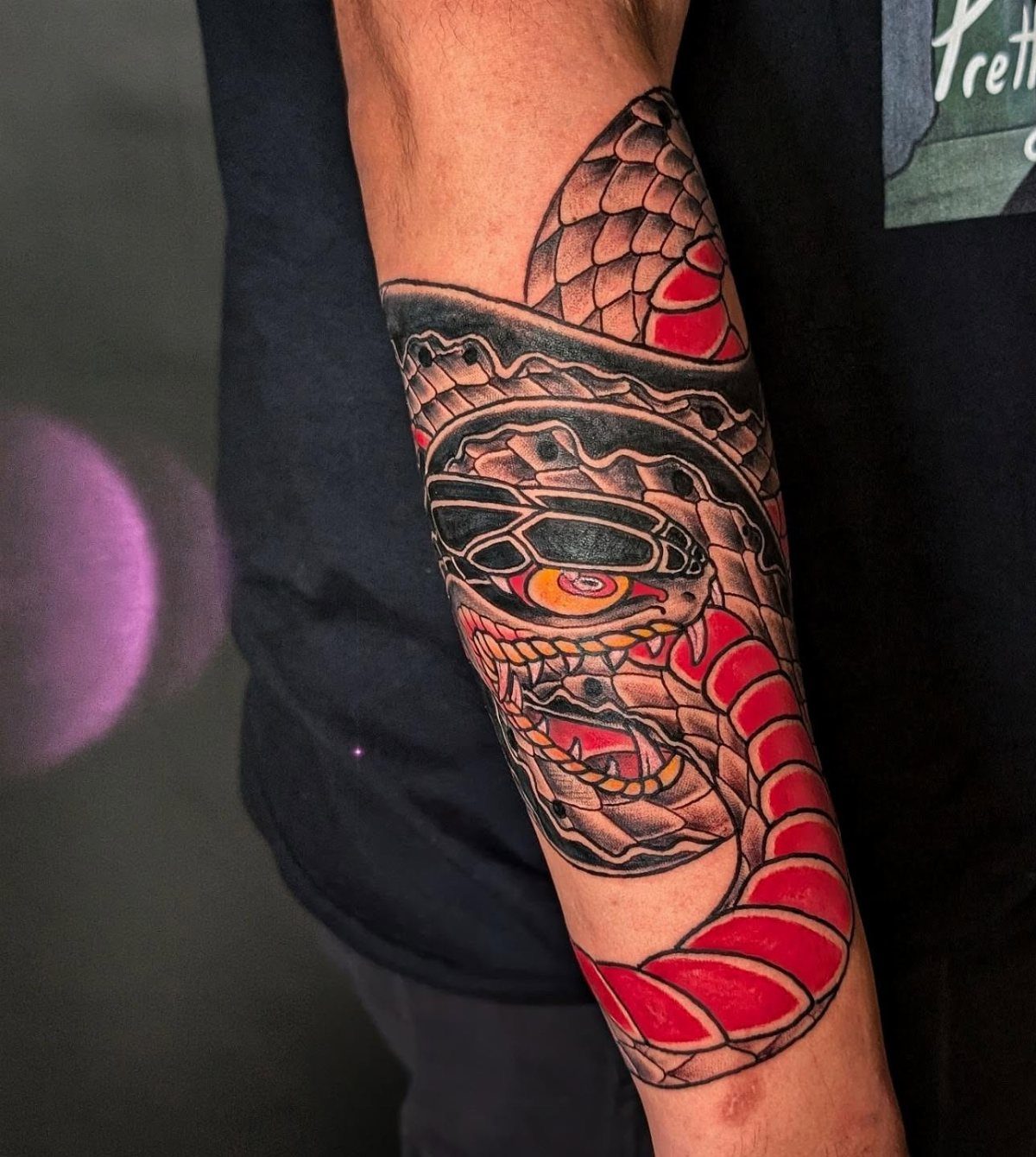Coiled snake tattoo with red scales and yellow eye on a person's forearm.