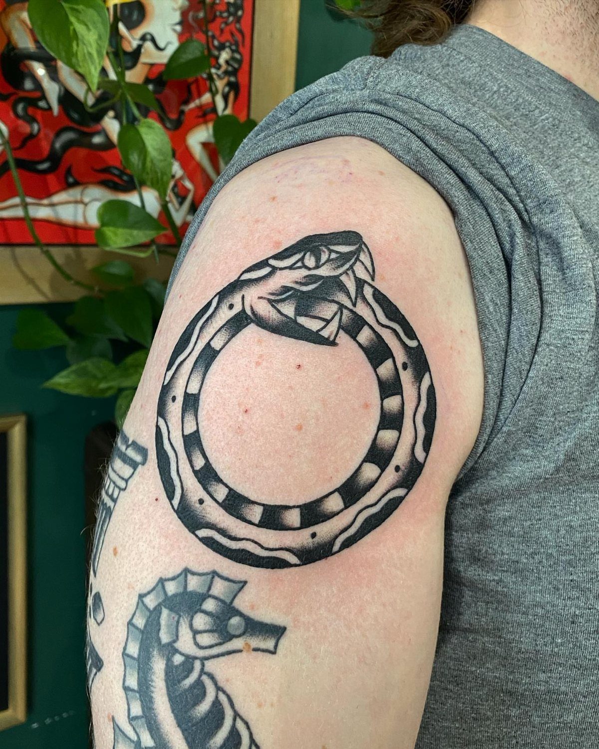 Ouroboros snake tattoo in traditional black and grey ink on a person's shoulder.