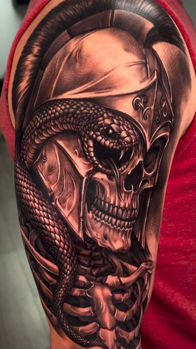 Skull and snake tattoo on an arm featuring a helmeted skull and coiled serpent.