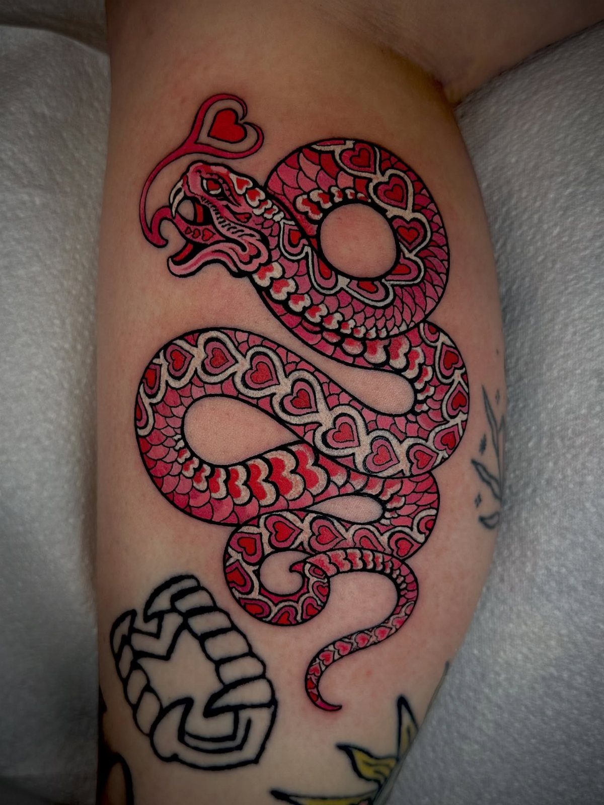 Red and pink coiled snake tattoo with heart-shaped scales and a floating heart.