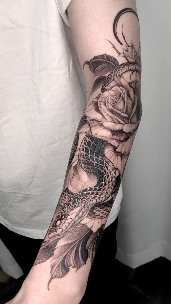 Snake coiled around a rose in a black and grey forearm tattoo.