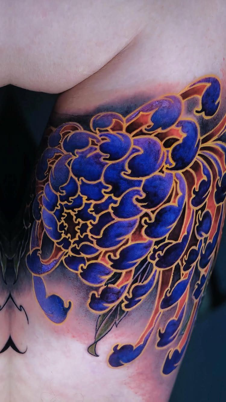Stylized blue chrysanthemum tattoo with orange outlines on a person's skin.