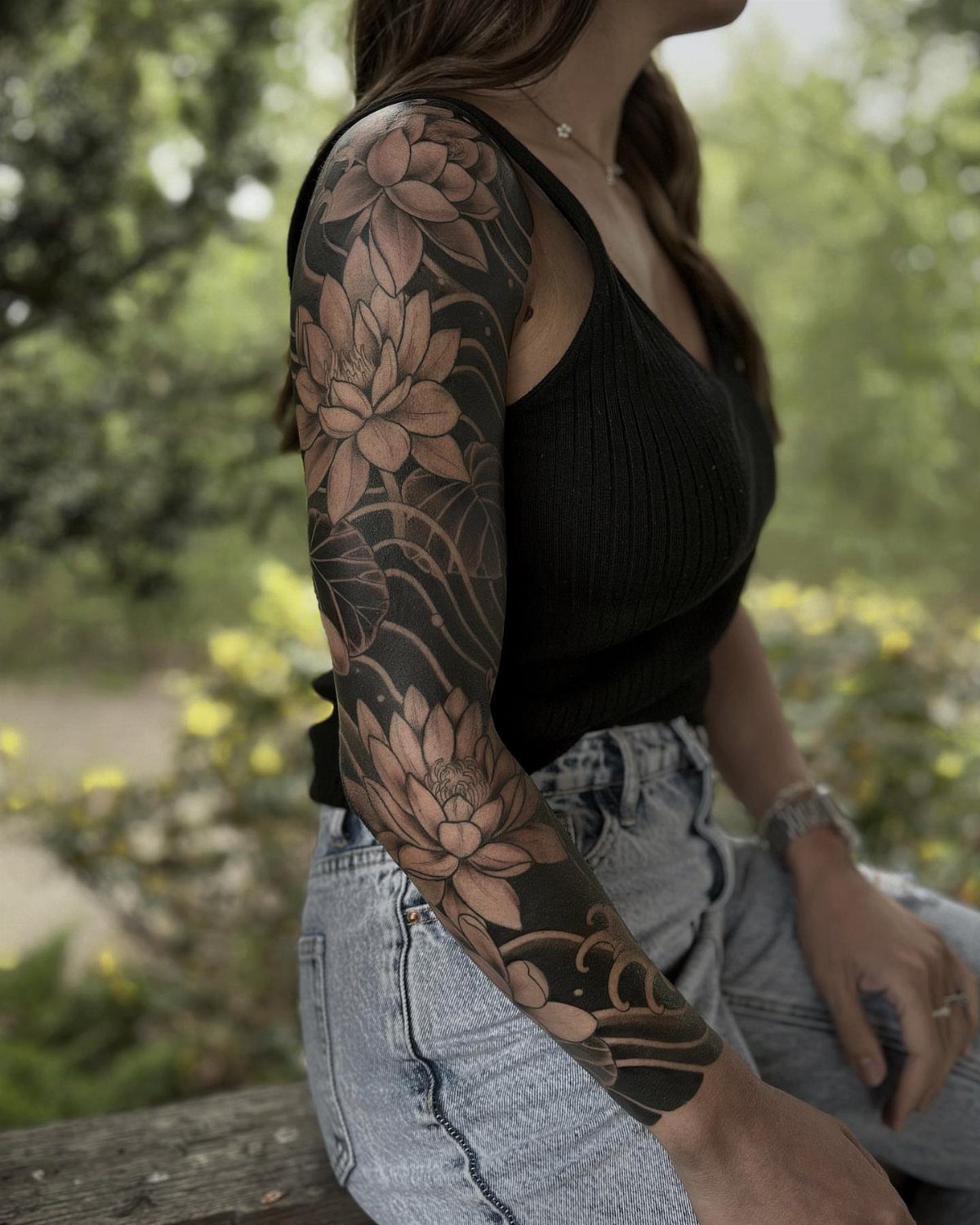 Woman with a full arm sleeve tattoo of lotus flowers and water waves.