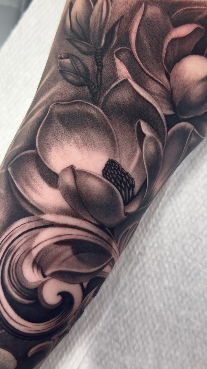Magnolia blossom tattoo in black and grey realism on a person's arm.