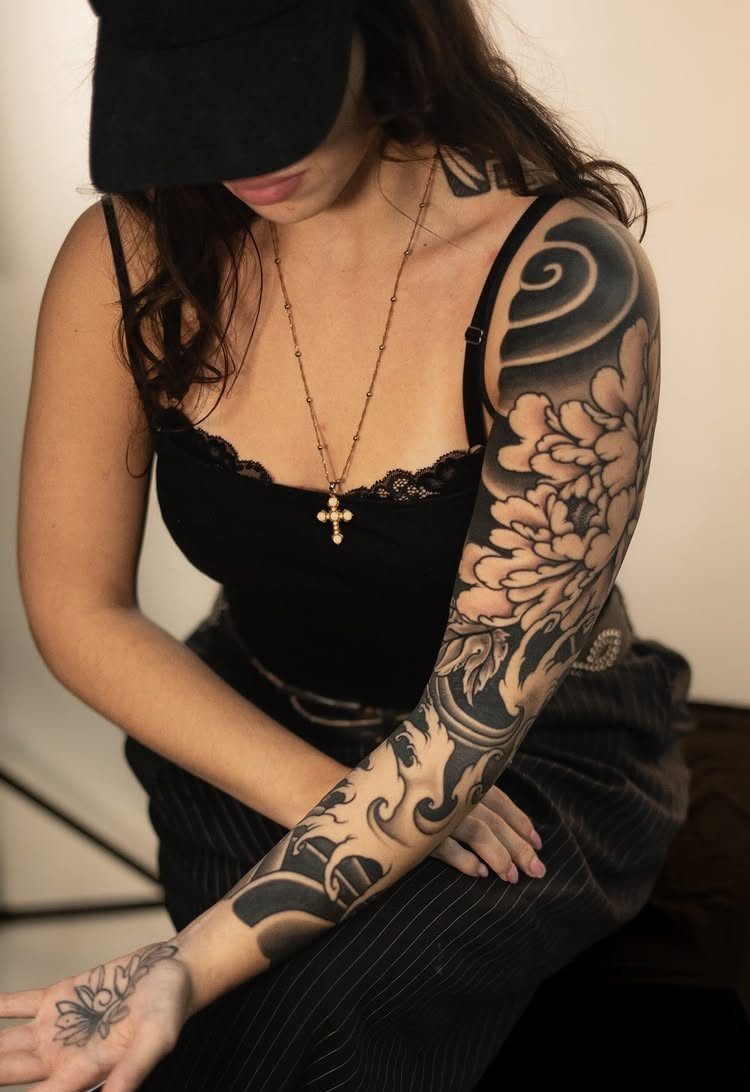 Peony blossom tattoo with waves covering a woman's arm in black and grey ink
