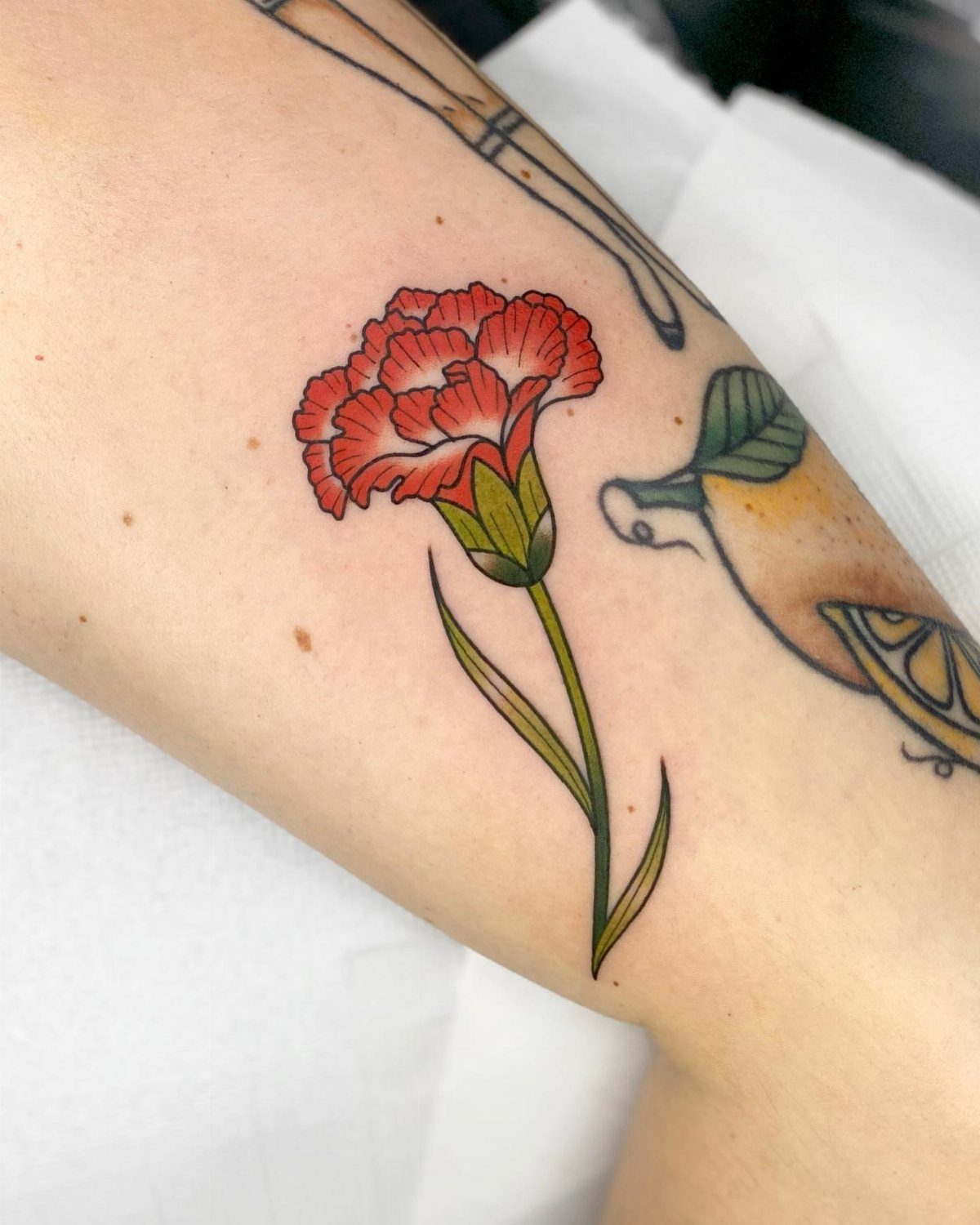 Red carnation tattoo with green stem and leaves on a person's arm.