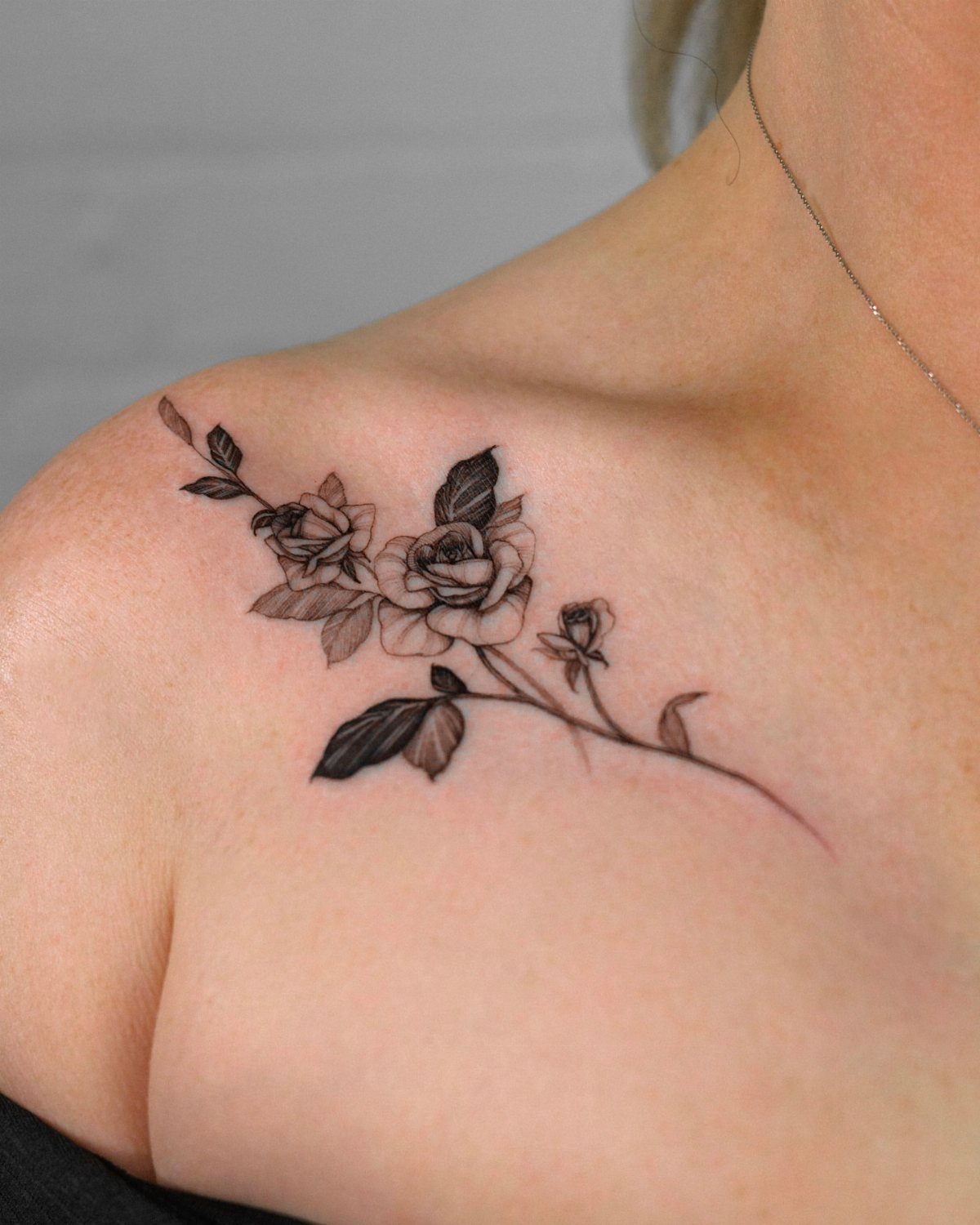 Black ink rose tattoo on a person's collarbone and shoulder area.