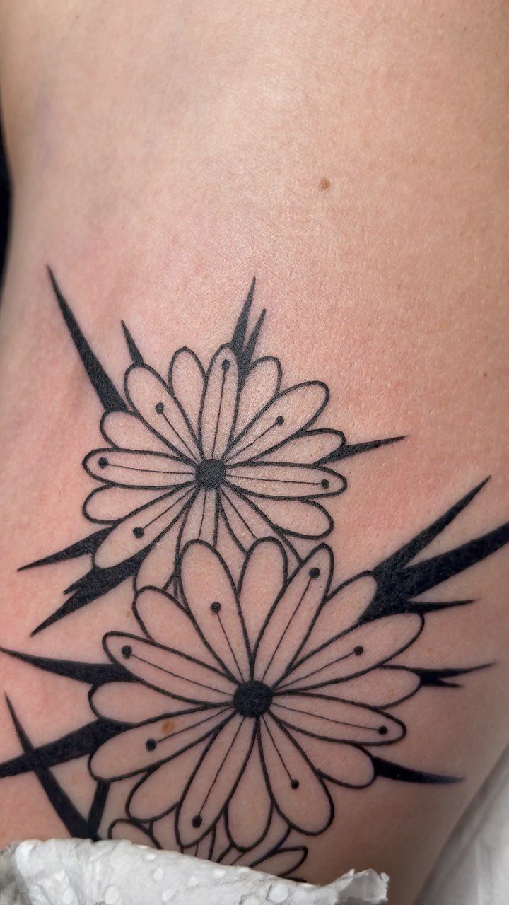 Two black ink daisy tattoos with bold outlines on a person's skin.