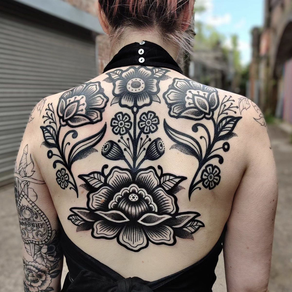 Large symmetrical black ink traditional flower tattoo covering a person's upper back.